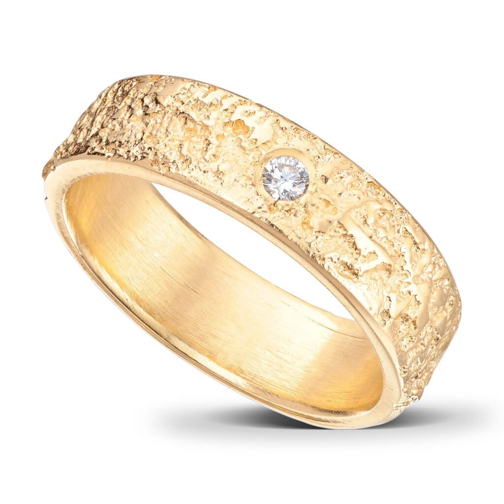 Ehering aus 14 Karat Gelbgold. 5 mm breit. Zerklüftete Oberfläche und gerade Kanten. Die Innenseite des Rings ist abgerundet, um ein angenehmes Tragegefühl zu gewährleisten. 1 Diamant.