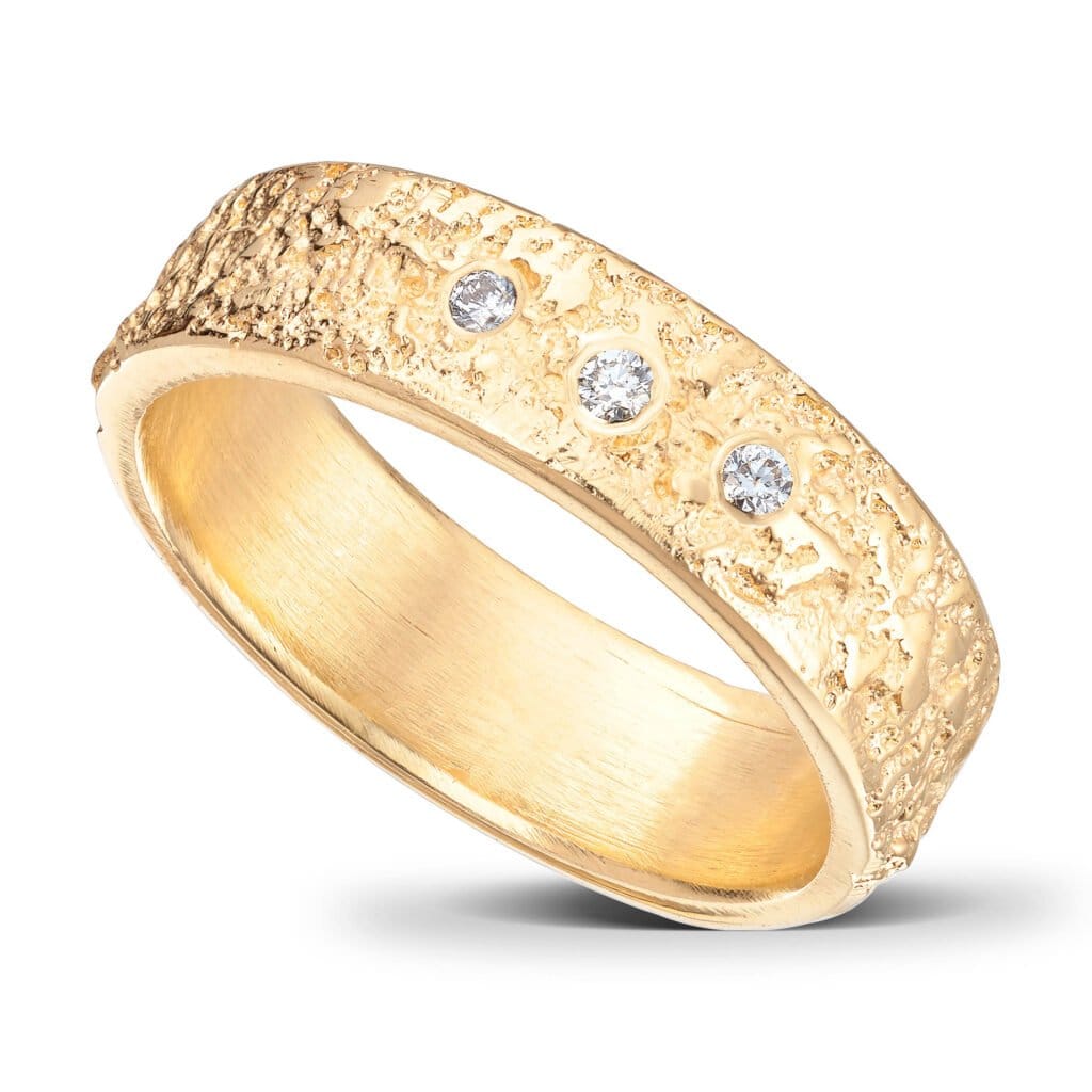 Ehering aus 14 Karat Gelbgold. 5 mm breit. Zerklüftete Oberfläche und gerade Kanten. Die Innenseite des Rings ist abgerundet, um ein angenehmes Tragegefühl zu gewährleisten. 3 Diamanten.
