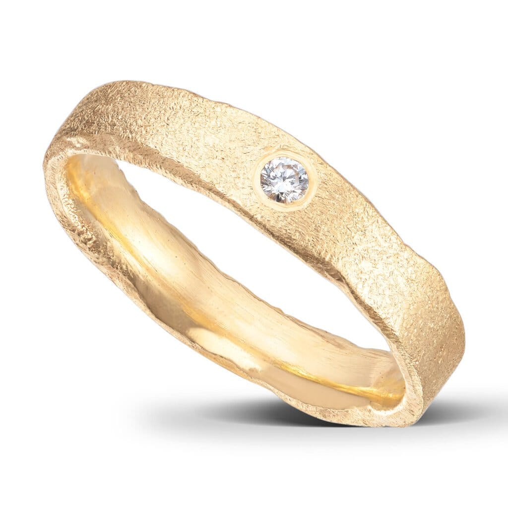 Schmaler und dünner Ehering. Gebürstete Oberfläche und unebene Seiten. 14 Karat Gelbgold. 1 Diamant.