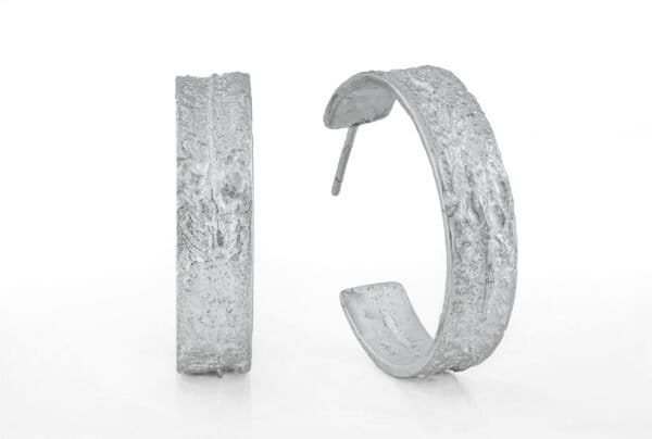 25 mm store øreringer i sølv, 8 mm bred. Ruglet overflate. Vekt ca. 7 gram per stk