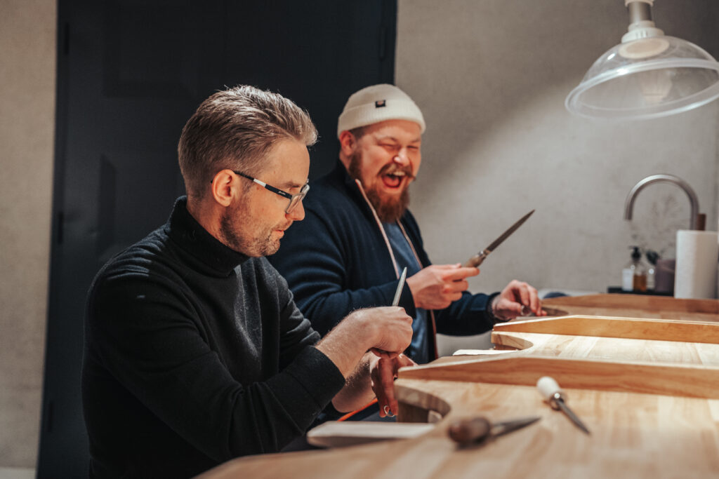 To menn smiler mens de lager sine egne sølvringer under Mingle Workshop hos Gallery Wabi Sabi i Tromsø.